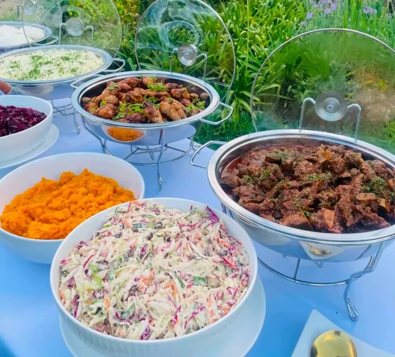 An outdoor buffet of chicken, beef stew, coleslaw, butternut and rice in a garden