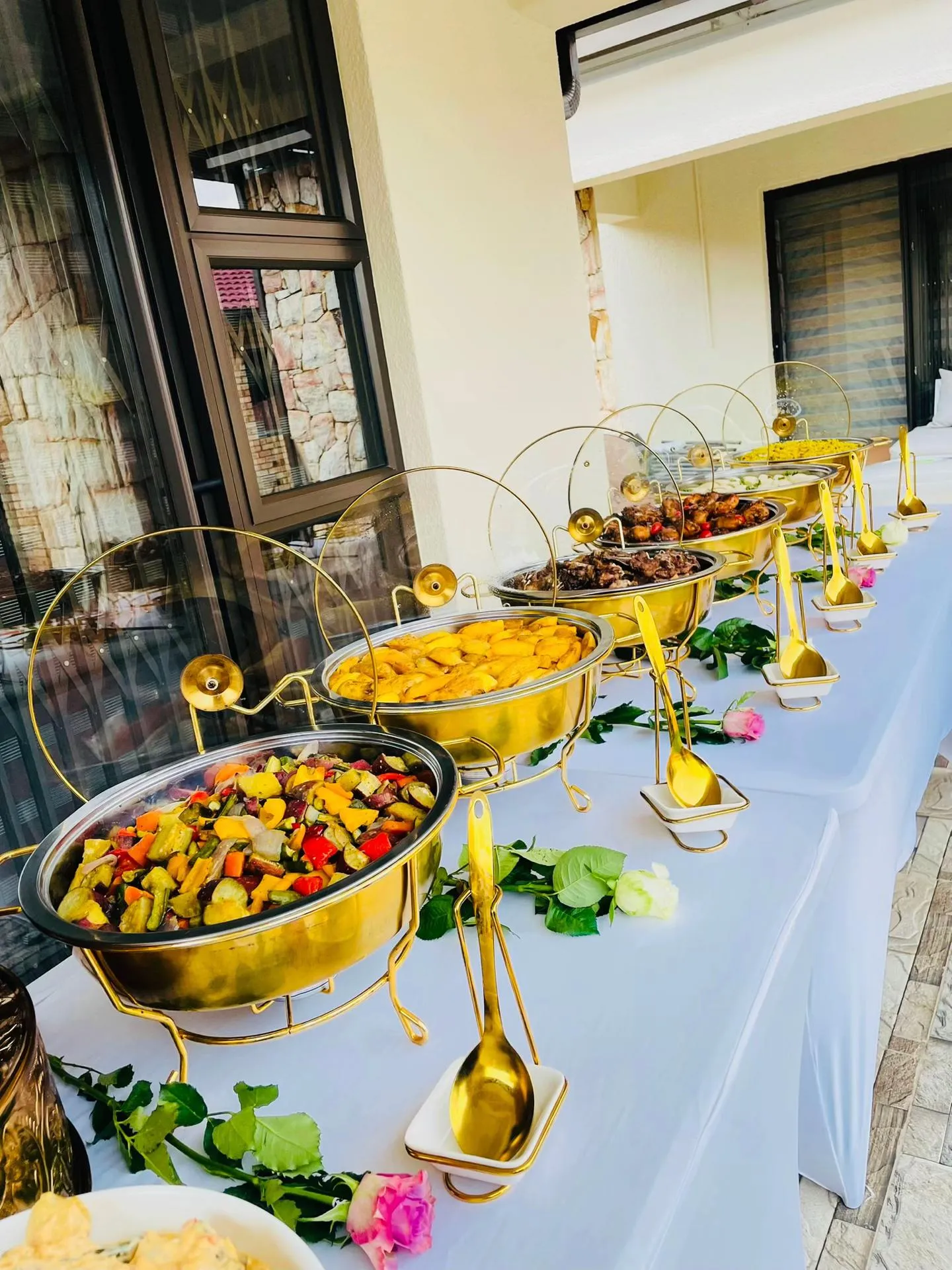 A buffet table with gold chafing dishes of roasted vegetables, potatoes and meat